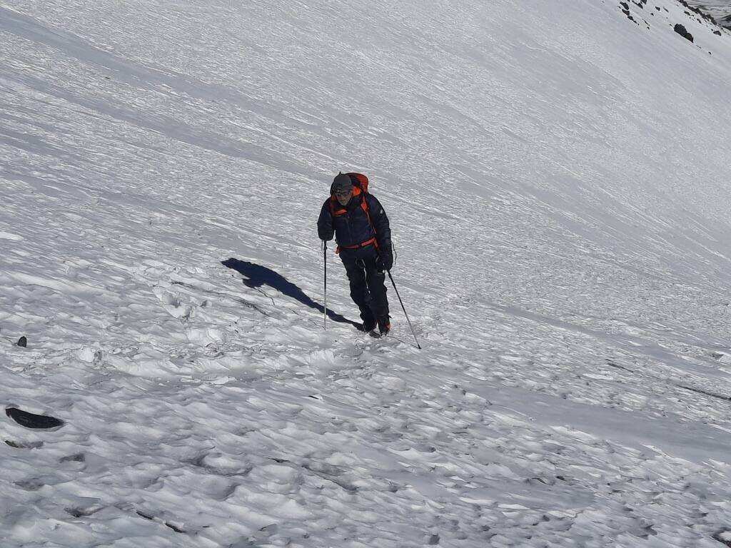 Climber moving up a long snow slope with trekking poles