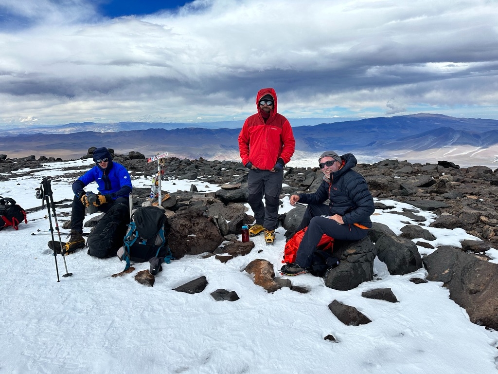 Three climbers at a summit marker high in the Atacama altiplano