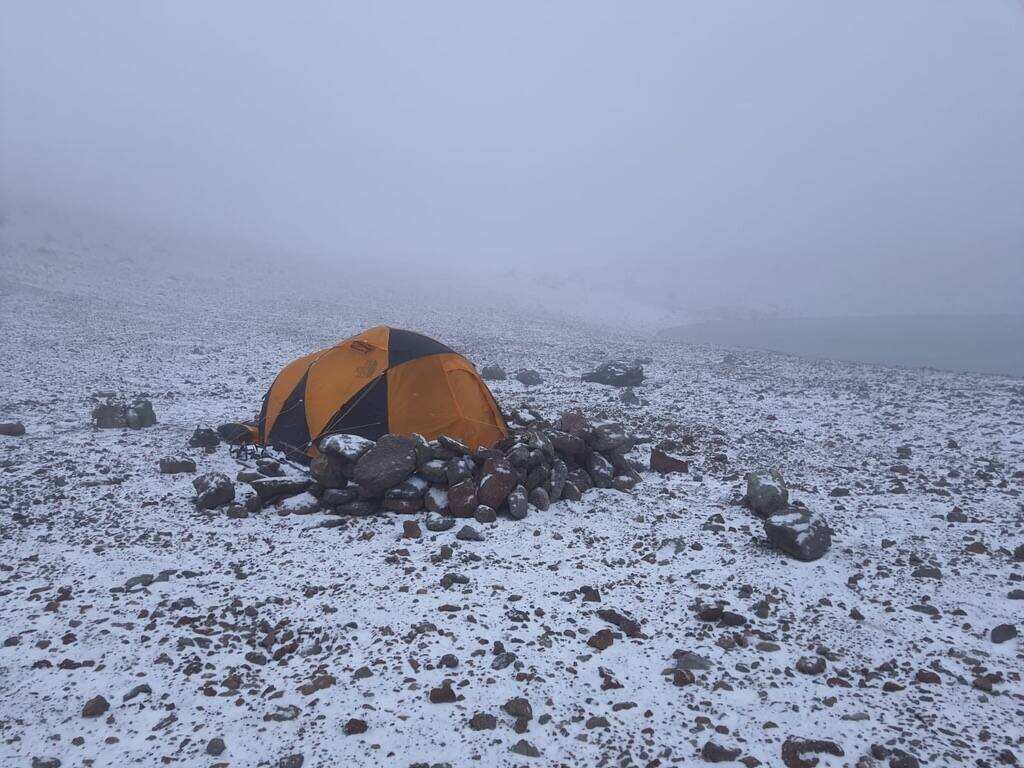 High camp tent anchored with rock walls in a fresh snow squall